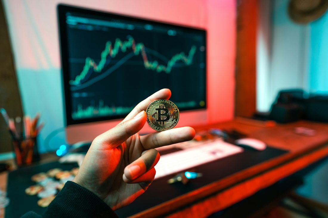 Holding a Bitcoin coin in front of a trading chart